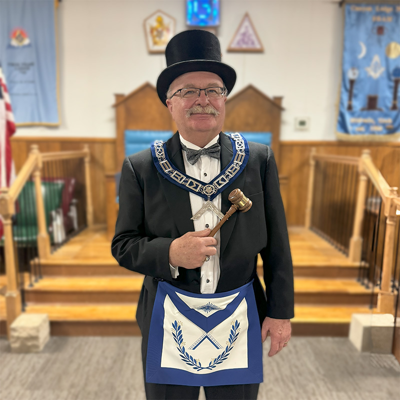 Robert Hartman as Worshipful Master wearing a top hat, square collar, and holding a gavel