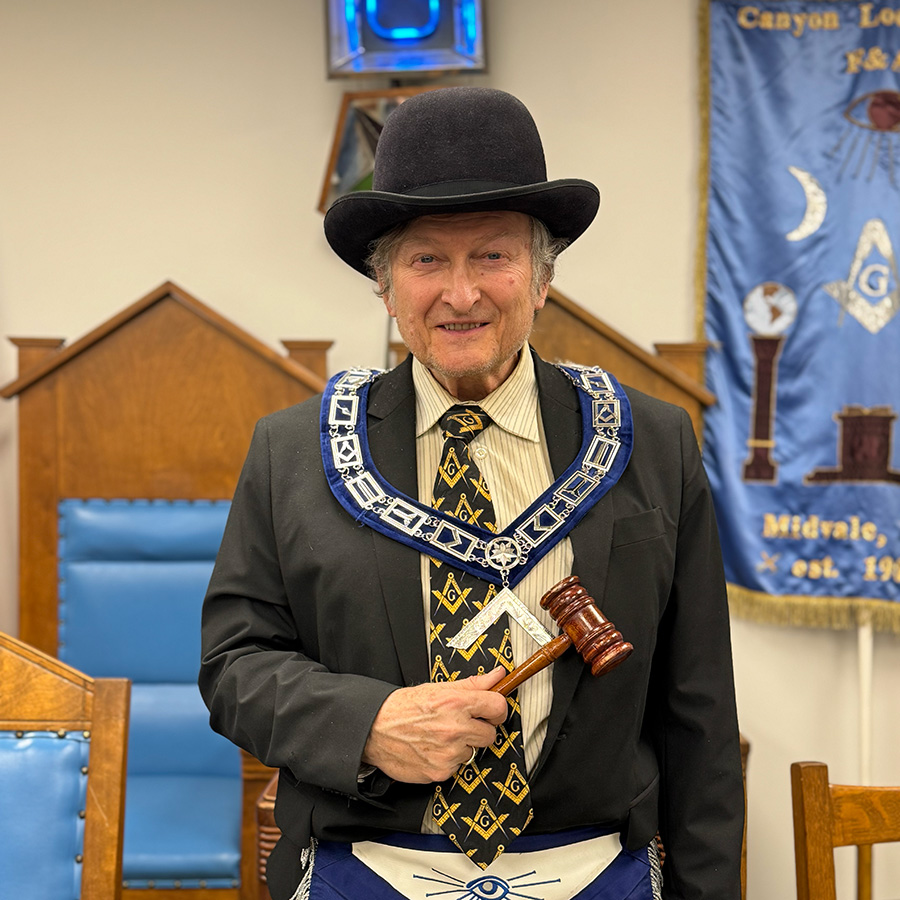 Lyle Millar as Worshipful Master wearing a hat, square collar, and holding a gavel
